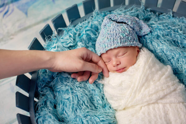 infant boy sleeping in a basket on a rug in a hat