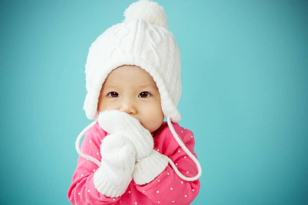 baby with white poodle hat and knitted mittens in winter season